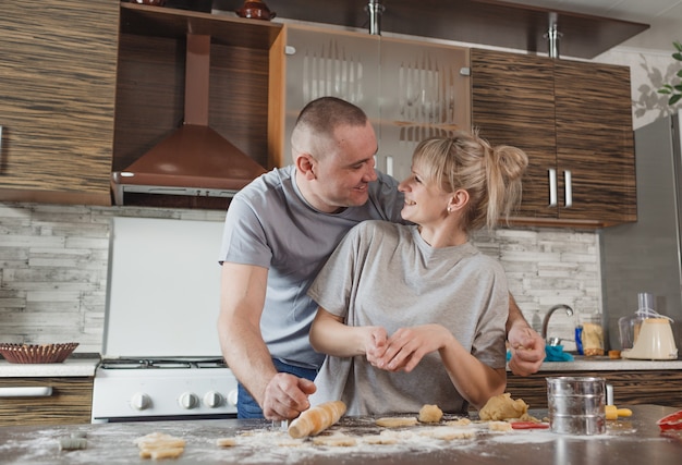 Glückliches junges Paar Ehemann und Ehefrau zusammen, die Spaß haben, Kekse zu Hause in der Küche zu machen. Freude und gegenseitiges Verständnis in der Familie.