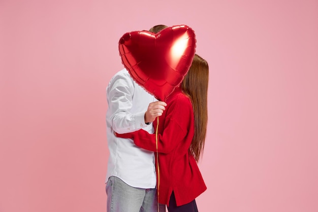 Glückliches junges Paar Frau und Mann halten einen Ballon in Herzform und küssen sich hinten gegen rosa