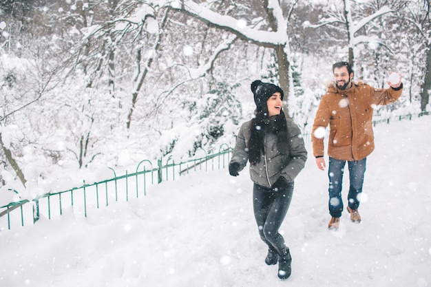 Glückliches junges Paar im Winter. Familie draußen. Mann und Frau, die aufwärts schauen und lachen. Liebe, Spaß, Jahreszeit und Leute - gehend in Winterpark. Er schneit