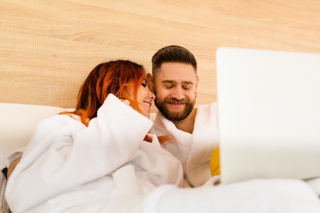 Glückliches junges Paar in Bademänteln liegt im Bett