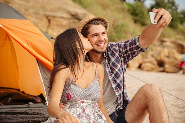 Glückliches junges Paar macht Selfie mit Smartphone und hat Spaß beim Campen am Strand