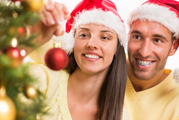 Glückliches junges Paar schmückt gerne den Weihnachtsbaum zu Hause. Selektiver Fokus, Fokus auf Paar.