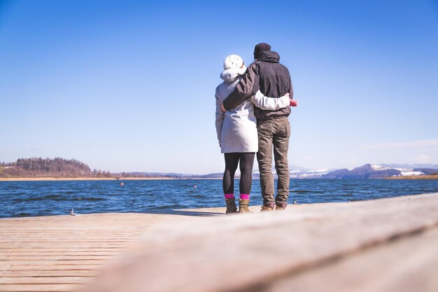 Glückliches junges Paar steht auf einer Fußgängerbrücke und genießt die Aussicht über die Winterzeit des Sees