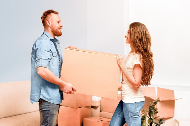 Glückliches junges Paar trägt Karton in den Händen beim Umzug in ein neues Zuhause