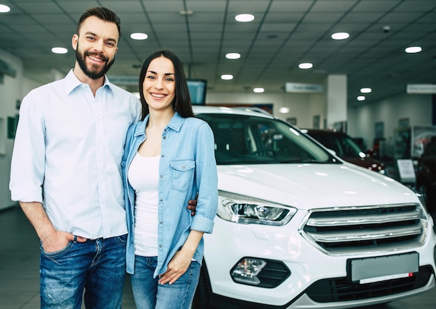Glückliches junges Paar wählt und kauft ein neues Auto für die Familie im Autohaus