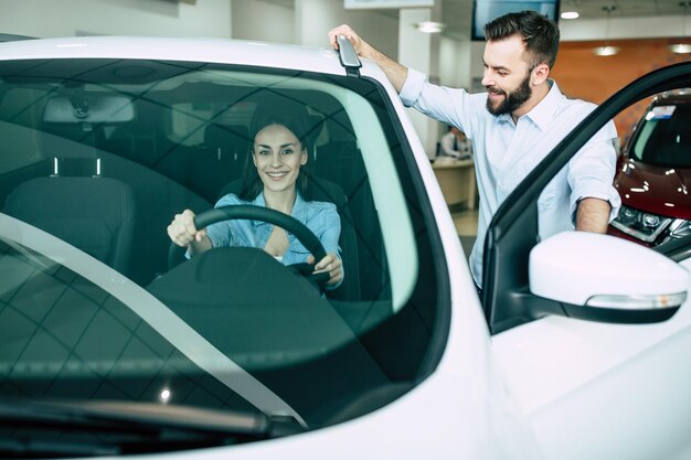 Glückliches junges Paar wählt und kauft ein neues Auto für die Familie im Autohaus