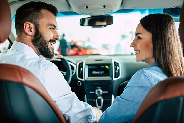 Glückliches junges Paar wählt und kauft ein neues Auto für die Familie im Autohaus