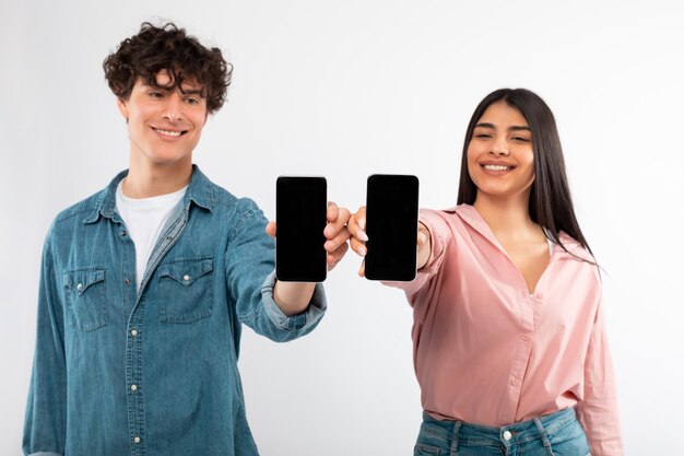 Glückliches junges Paar zeigt Smartphones mit leeren Bildschirmen und weißem Hintergrund