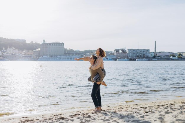 Glückliches junges Paar zu Fuß am Strand Gut aussehender Kerl trägt ein Mädchen in seinen Armen Liebendes Paar, das Spaß hat, lachen sie, indem sie sich umarmen