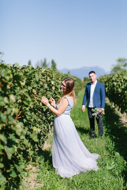 Glückliches junges schönes Paar in den blauen Kleidern, die im Garten am sonnigen Tag gehen. Paar in der Liebe lächelnd, umarmend und küssend auf dem Hintergrund des schönen Weinbergs in Italien