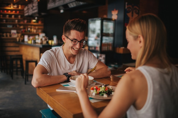 Glückliches junges verliebtes Paar, das ein schönes Date in einer Bar oder einem Restaurant hat. Sie erzählen Geschichten über sich selbst, trinken Tee oder Kaffee und essen Salat und Suppe