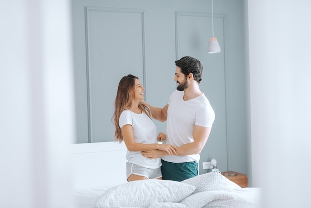 Glückliches kaukasisches Paar im Pyjama, das am Morgen im Bett lächelt und umarmt. Schlafzimmer Interieur.