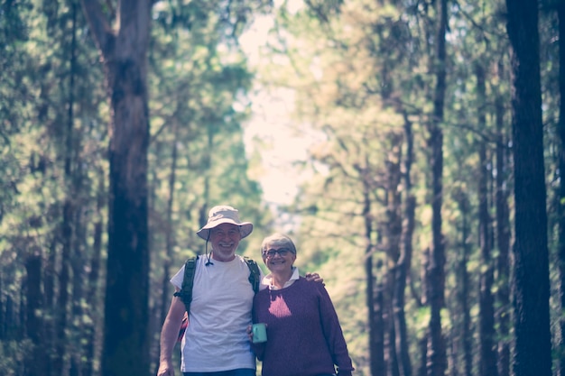 Glückliches kaukasisches Seniorenpaar lächelt und genießt die Reise mit Rucksack im Naturwald im Freien - alternatives kostenloses Urlaubskonzept für ältere Menschen - fröhlicher Lebensstil und Umarmung und Liebe and