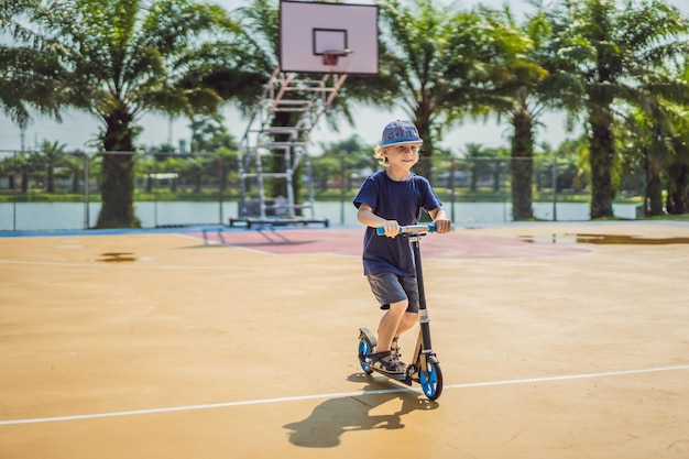 Glückliches Kind auf Tretroller auf dem Basketballplatz Kinder lernen, Rollbrett kleiner Junge zu skaten