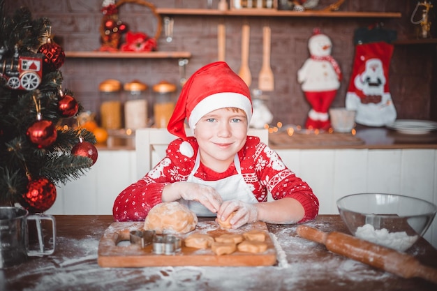 Glückliches Kind bereitet festliche Weihnachtskekse in der Küche des Hauses an Heiligabend vor Frohe Weihnachten und frohe Neujahrsferien mit der Familie