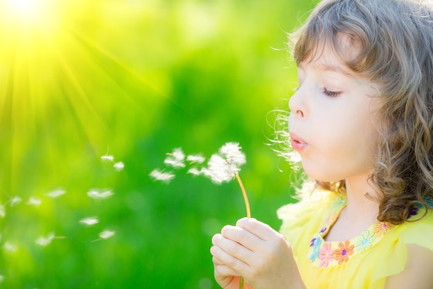 glückliches Kind bläst Löwenzahnblume im Freien Mädchen, das Spaß im Frühlingstraum und -phantasie hat