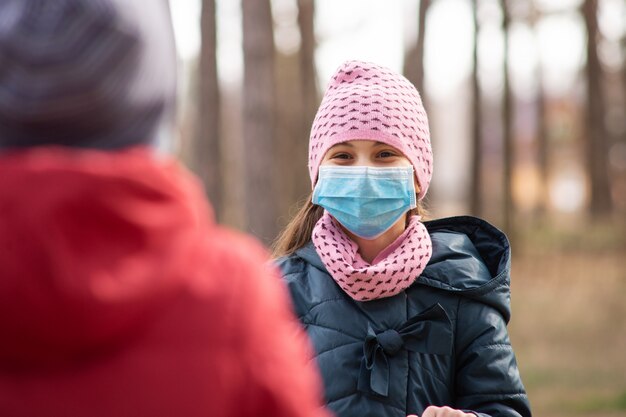 Glückliches Kind, das auf Spielplatz spielt, der medizinische Maske trägt, um sich vor dem gefährlichen Covid-19-Virus zu schützen, gefährliches Spielen während des Ausbruchs des Coronavirus