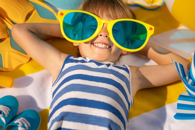 Glückliches Kind, das auf Strandtuch liegt Lustiges Kind im Freien in den Sommerferien