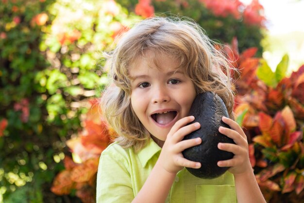 Glückliches Kind, das Avocado im Sommergarten zeigt. Gesundes Essen für Kinder.