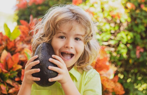 Glückliches Kind, das Avocado im Sommergarten zeigt. Kinder gesundes essen.