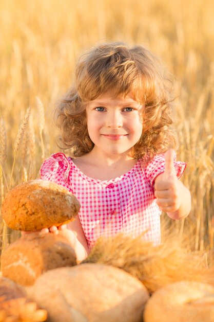 Glückliches Kind, das Brot gegen gelbes Herbstweizenfeld hält