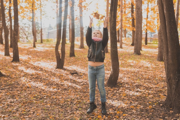 Glückliches Kind, das die gefallenen Blätter beim Spielen im Herbstpark wirft.