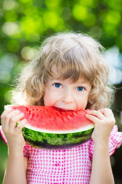 Glückliches kind, das draußen im sommerpark wassermelone isst