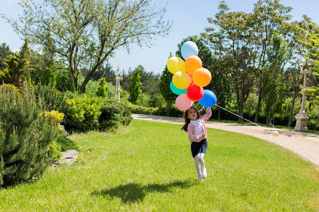 Glückliches Kind, das draußen mit bunten Spielzeugballons springt Lächelndes Kind, das Spaß im grünen Gras hat