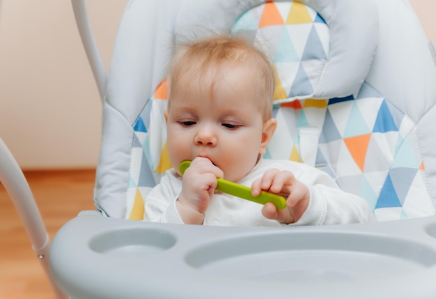 Glückliches Kind, das einen Löffel in einem Hochstuhl hält, Babynahrung