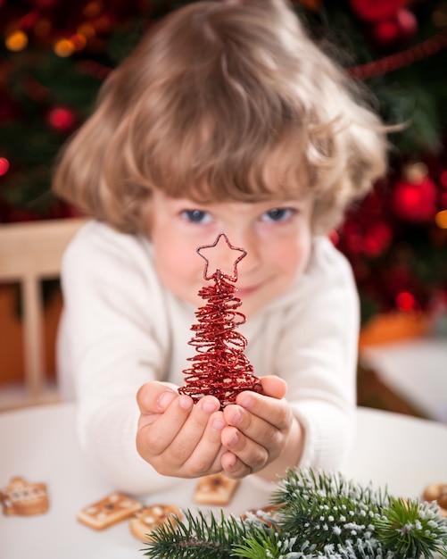 Glückliches Kind, das handgemachte Dekoration gegen Weihnachtsbeleuchtung hält. Fokus auf Vordergrund