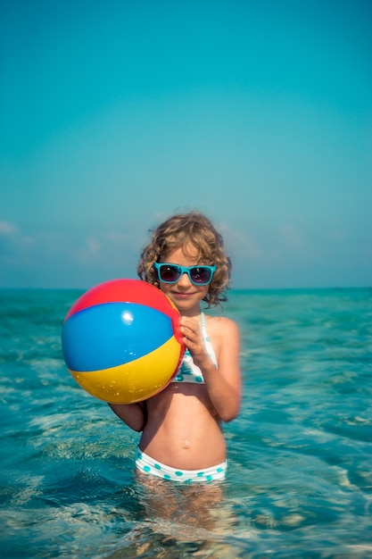 glückliches Kind, das im Meer mit einem bunten aufblasbaren Ball spielt