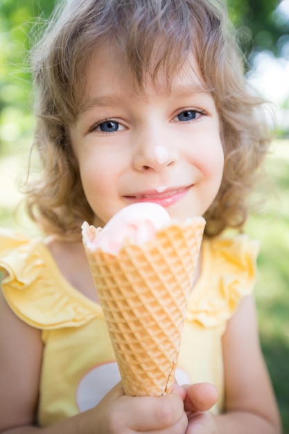 Glückliches Kind, das im Sommerpark Eis im Freien isst