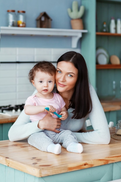 Glückliches Kind, das in der Küche am Tisch mit Mutter sitzt, die einen Löffel in seiner Hand hält