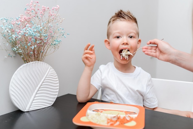 Glückliches Kind, das köstliche Pasta am Tisch in der Küche isst