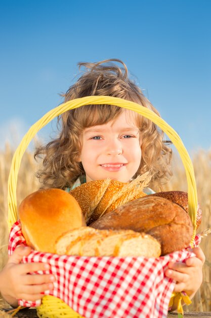 Glückliches Kind, das Korb mit Brot im gelben Herbstweizenfeld gegen Hintergrund des blauen Himmels hält