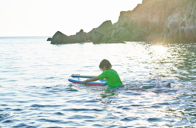 Glückliches Kind, das mit Bodyboard im Meer spielt. Kind hat Spaß im Freien. Konzept der Sommerferien und des gesunden Lebensstils.