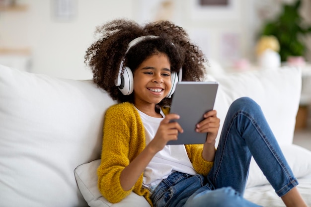 Foto glückliches kind, das mit digitalem tablet und headset auf der couch sitzt