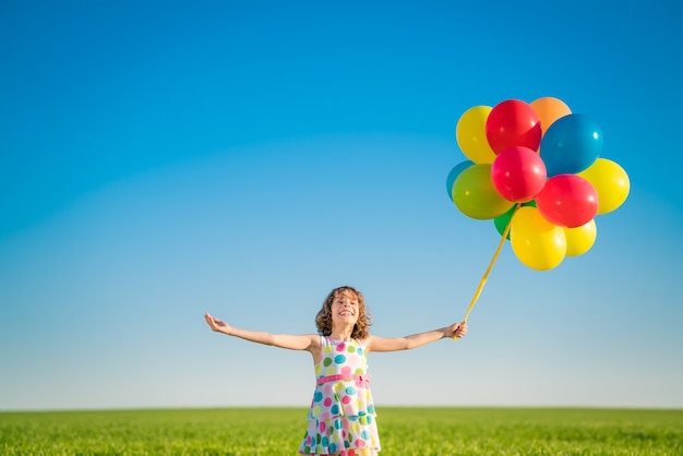 Glückliches Kind, das mit hellen mehrfarbigen Luftballons im Freien spielt