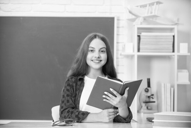 Glückliches Kind, das mit Schreibheft im Klassenzimmer am Tafelwissen sitzt