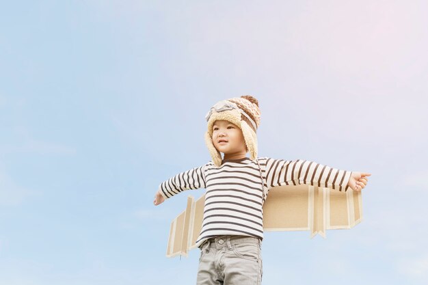 Glückliches Kind, das mit Spielzeugflügeln gegen Sommerhimmelhintergrund spielt
