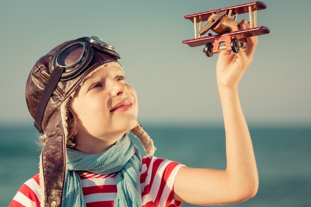 glückliches Kind, das mit Spielzeugflugzeug gegen Meer- und Himmelhintergrund spielt