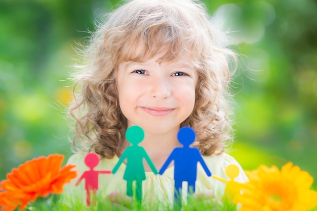 Glückliches Kind, das Papierfamilie in den Händen gegen frühlingsgrünen Hintergrund hält