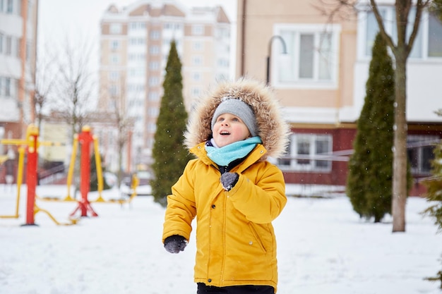 Glückliches Kind, das Spaß im Schnee in der Stadt hat Winterspaß außerhalb Boy in leuchtend orange Winterjacke