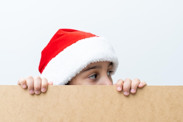 Glückliches Kind des kleinen Mädchens in Sankt-Hut, das hinter leerem Zeichenbanner späht. Verkauf, Feiertage, Weihnachten, Neujahrskonzept