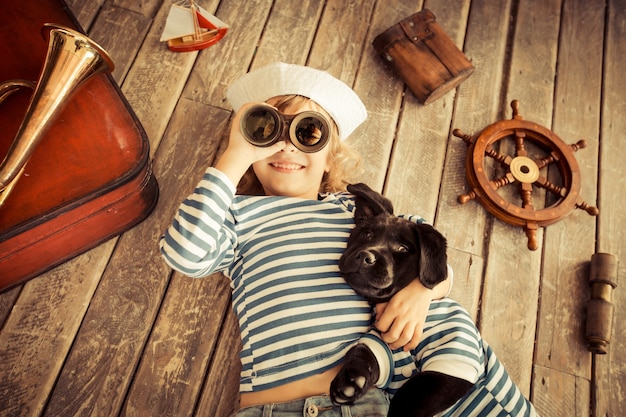 Glückliches Kind gekleidet im Seemann. Kind, das zu Hause mit Hund spielt Reise- und Abenteuerkonzept