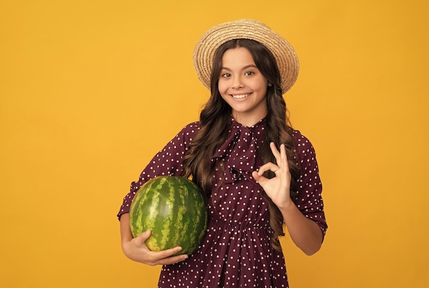 Glückliches Kind hält frische reife Wassermelonenfrüchte im Sommerstrohhut mit ok Gestenernährung