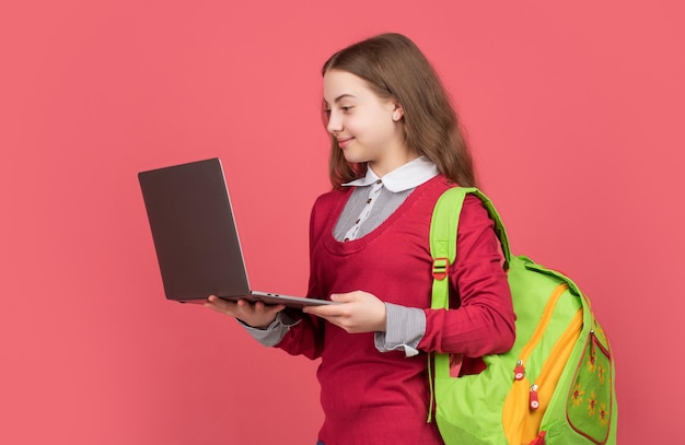 Glückliches Kind hält Laptop mit Rucksack auf rotem Hintergrund