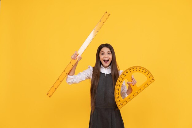 Glückliches Kind hält Mathe-Winkelmesser und Lineal in der Schule auf gelbem Hintergrund, Bildung.