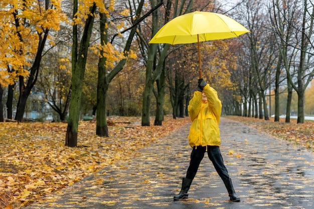 Glückliches Kind im gelben Regenmantel im Park mit gelbem Regenschirm Spaziergang mit Kind in regnerischer Herbststraße