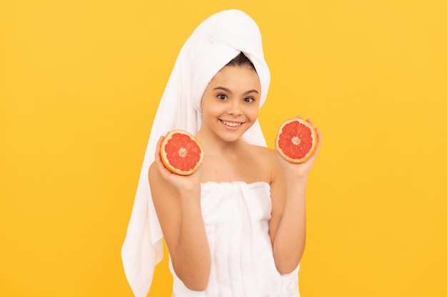 Glückliches Kind im Handtuch mit Grapefruit auf gelbem Hintergrund